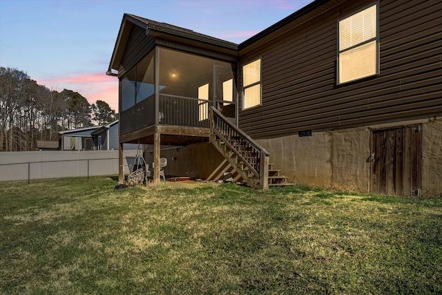 back of property at dusk featuring a sunroom, fence, stairway, and a lawn