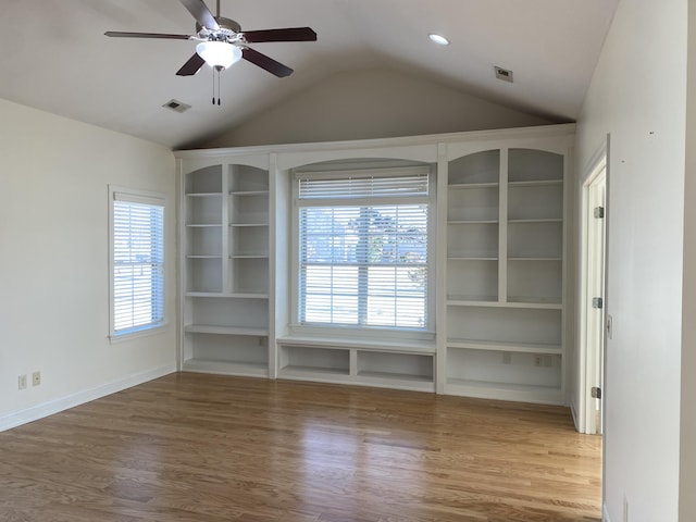 empty room featuring built in features, a wealth of natural light, and hardwood / wood-style floors