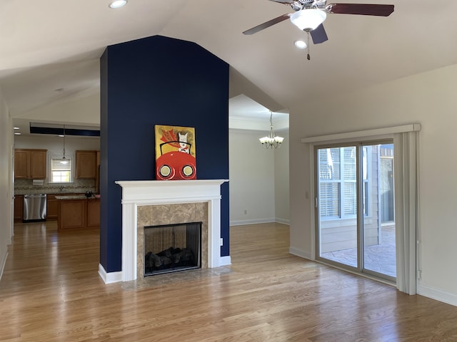 unfurnished living room with lofted ceiling, light wood-type flooring, a tiled fireplace, and ceiling fan with notable chandelier