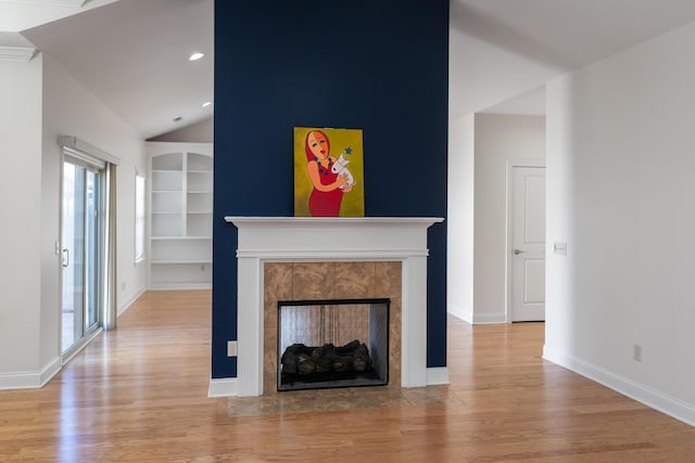 unfurnished living room with a tiled fireplace, vaulted ceiling, built in features, and light hardwood / wood-style flooring