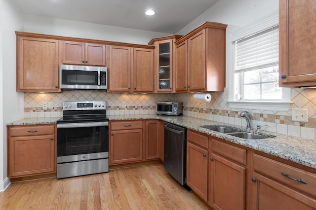 kitchen with light stone counters, appliances with stainless steel finishes, light hardwood / wood-style flooring, and sink