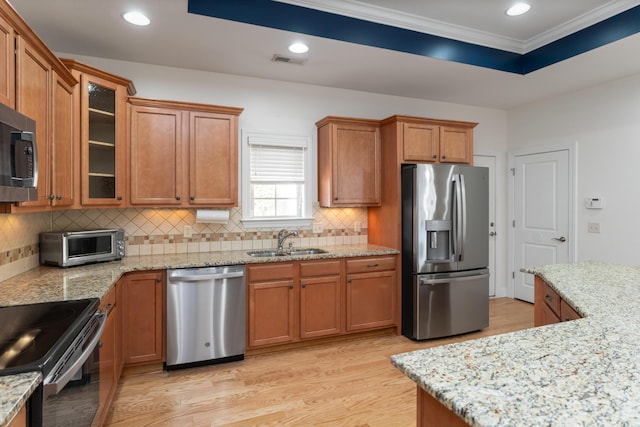 kitchen featuring light stone countertops, light wood-type flooring, appliances with stainless steel finishes, and sink