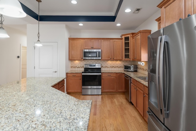 kitchen with a raised ceiling, stainless steel appliances, light stone countertops, decorative light fixtures, and backsplash