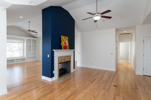 unfurnished living room with lofted ceiling, a tiled fireplace, light wood-type flooring, and built in features