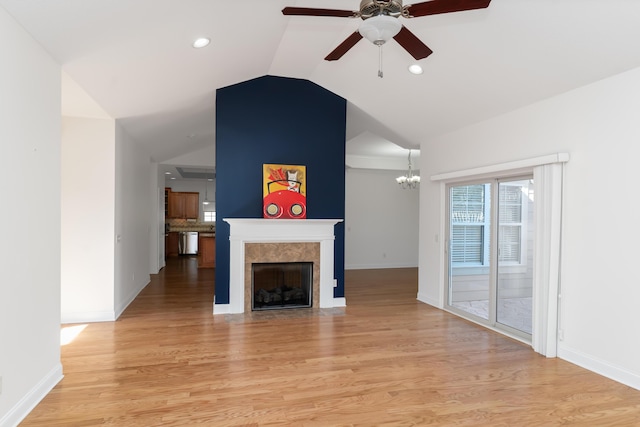 unfurnished living room with ceiling fan with notable chandelier, vaulted ceiling, and light hardwood / wood-style flooring