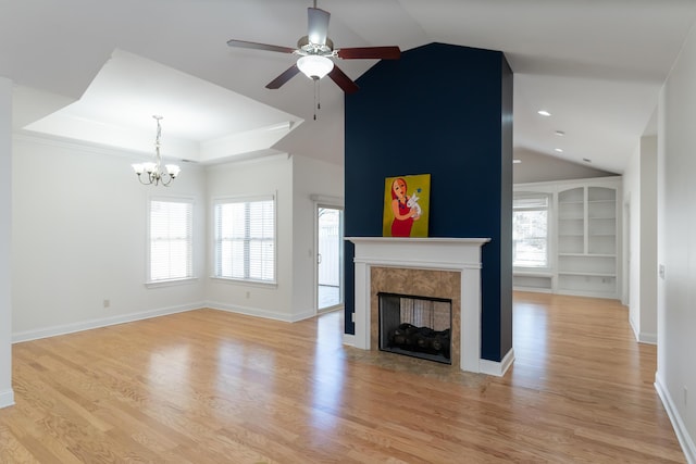 unfurnished living room featuring a premium fireplace, light hardwood / wood-style flooring, ceiling fan with notable chandelier, and built in shelves