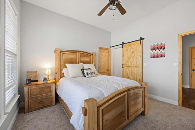 bedroom featuring ceiling fan, light colored carpet, multiple windows, and a barn door