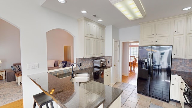 kitchen with sink, kitchen peninsula, dark stone countertops, decorative backsplash, and black appliances