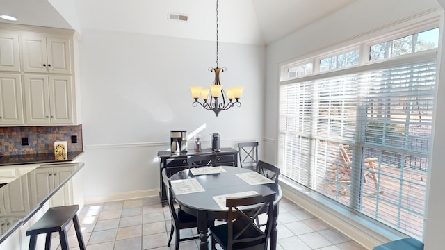 tiled dining space featuring an inviting chandelier and vaulted ceiling