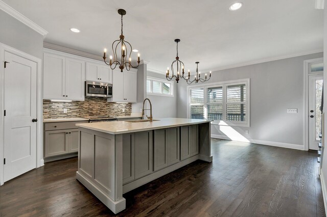 kitchen featuring decorative light fixtures, an inviting chandelier, an island with sink, sink, and crown molding