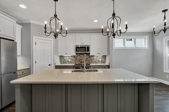 kitchen with light stone countertops, hanging light fixtures, appliances with stainless steel finishes, and a kitchen island with sink