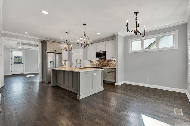 kitchen with stainless steel appliances, backsplash, a notable chandelier, a kitchen island with sink, and pendant lighting