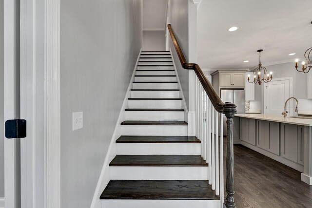 stairs with sink, wood-type flooring, ornamental molding, and a notable chandelier