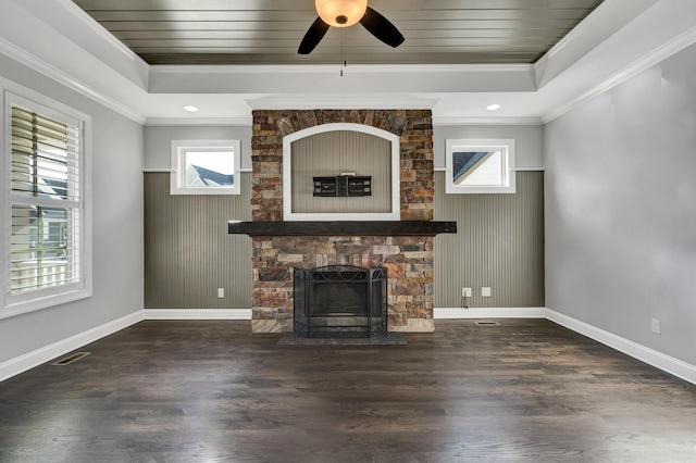 unfurnished living room featuring a tray ceiling, dark hardwood / wood-style floors, ornamental molding, and a stone fireplace