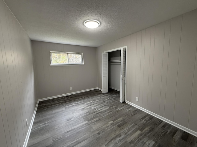 unfurnished bedroom featuring wood walls, dark wood-type flooring, and a closet