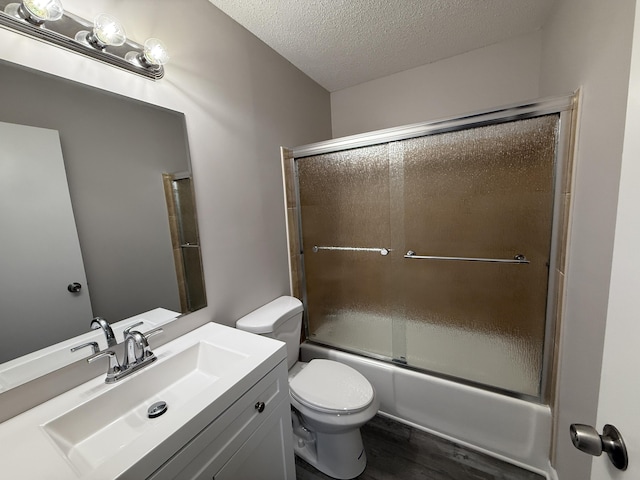 full bathroom with combined bath / shower with glass door, a textured ceiling, toilet, vanity, and hardwood / wood-style flooring