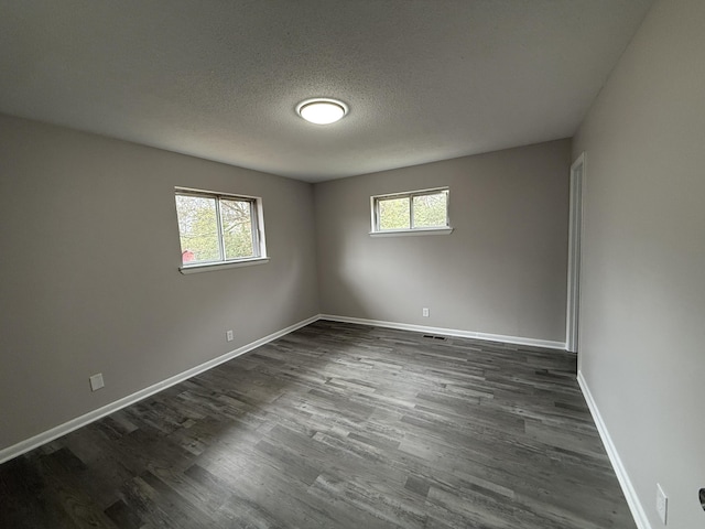 empty room featuring dark hardwood / wood-style floors, a textured ceiling, and a wealth of natural light