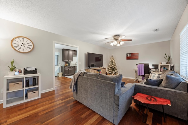 living room with a textured ceiling, ceiling fan, and dark wood-type flooring