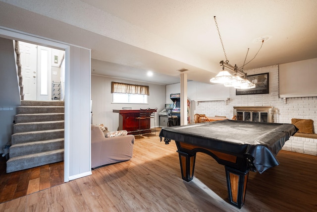 rec room featuring brick wall, wood-type flooring, a fireplace, and billiards