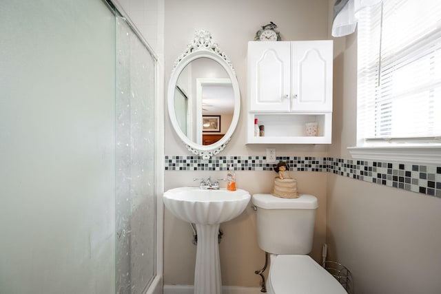 bathroom featuring toilet, a shower with door, and backsplash