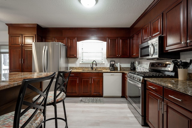 kitchen with dark stone counters, sink, a textured ceiling, light hardwood / wood-style floors, and stainless steel appliances