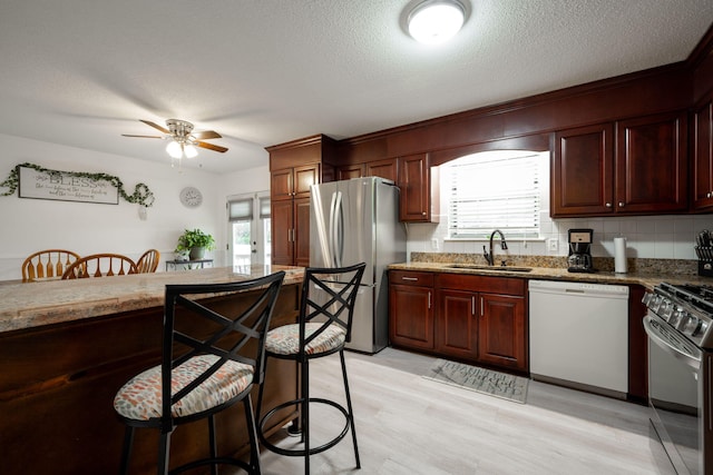 kitchen featuring stone counters, sink, light hardwood / wood-style flooring, appliances with stainless steel finishes, and a kitchen bar