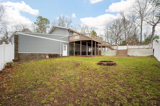 rear view of property featuring an outdoor fire pit, a yard, and a deck