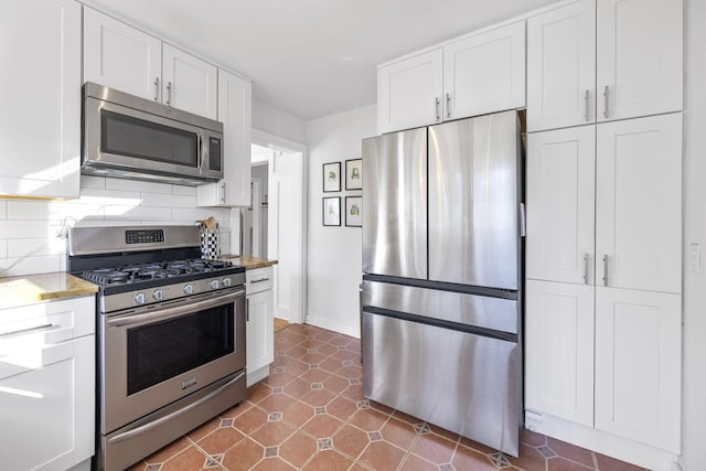 kitchen featuring white cabinets, stainless steel appliances, dark tile patterned flooring, and tasteful backsplash