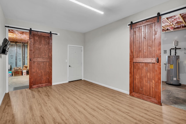 empty room with a barn door, electric water heater, and light hardwood / wood-style floors