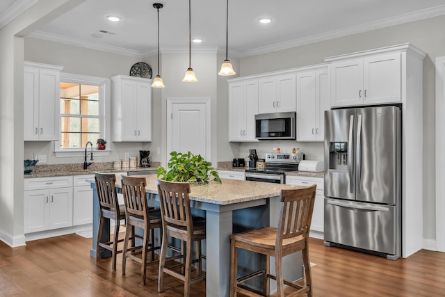 kitchen featuring pendant lighting, appliances with stainless steel finishes, white cabinetry, light stone counters, and a kitchen island