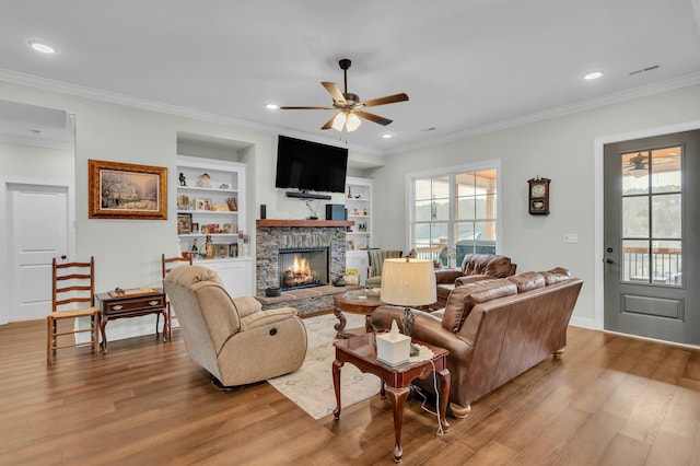 living room featuring crown molding, a fireplace, built in features, and ceiling fan