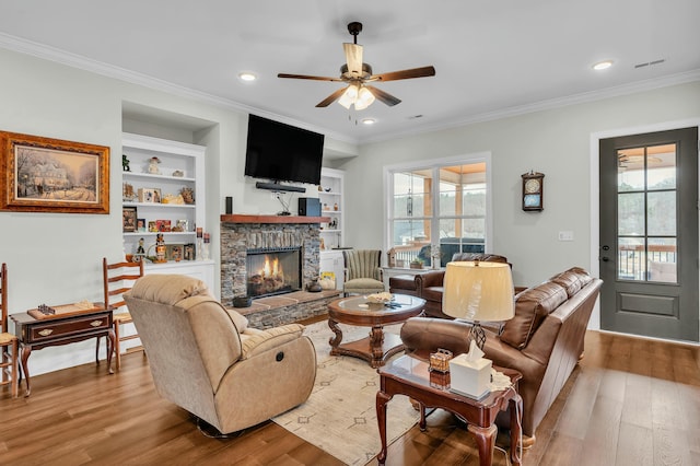 living room with built in shelves, ceiling fan, a fireplace, and crown molding