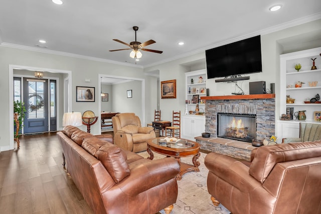 living room featuring crown molding, a stone fireplace, built in features, and light hardwood / wood-style floors