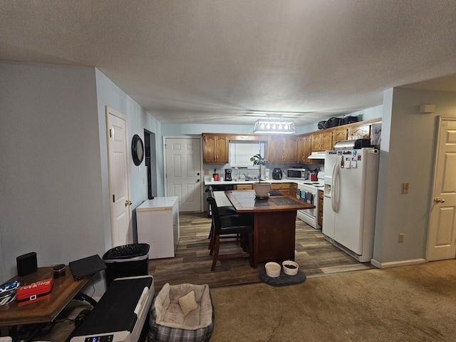 kitchen with a breakfast bar, white appliances, dark colored carpet, a textured ceiling, and a kitchen island