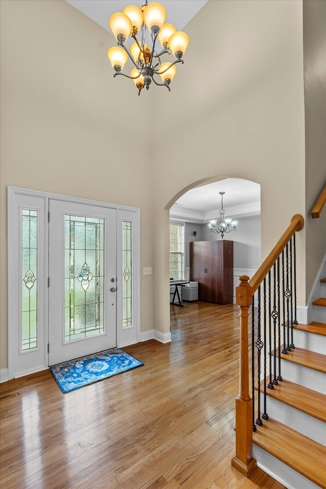 entryway with a chandelier, a towering ceiling, light wood-type flooring, and a healthy amount of sunlight