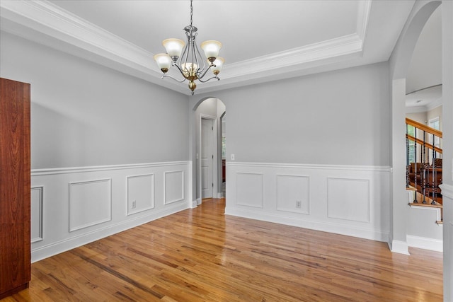 empty room featuring light hardwood / wood-style floors, a raised ceiling, crown molding, and an inviting chandelier