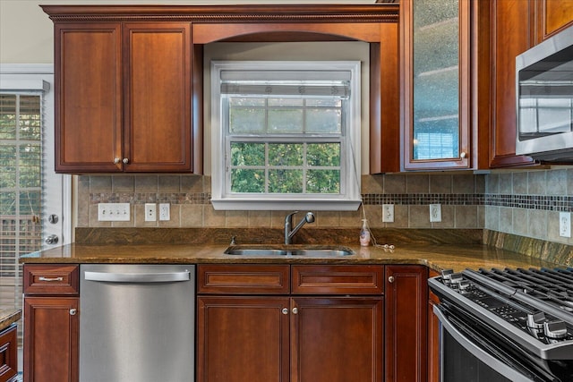 kitchen with appliances with stainless steel finishes, backsplash, dark stone counters, and sink