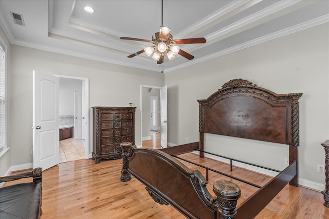 bedroom with crown molding, ceiling fan, light wood-type flooring, connected bathroom, and a tray ceiling