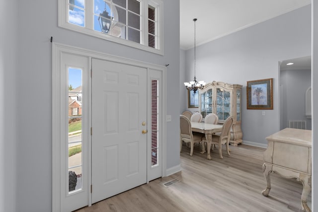 entryway with a healthy amount of sunlight, light hardwood / wood-style flooring, ornamental molding, and a notable chandelier