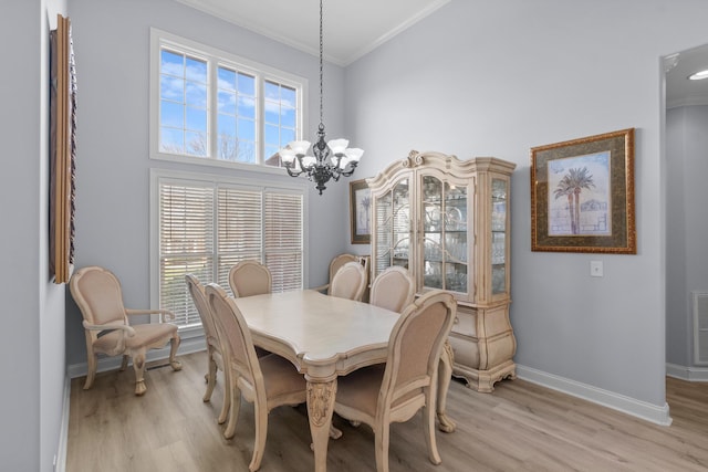 dining space with a towering ceiling, an inviting chandelier, light wood-type flooring, and ornamental molding