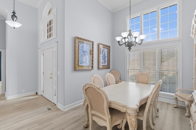 dining room featuring light hardwood / wood-style floors, a towering ceiling, crown molding, and an inviting chandelier