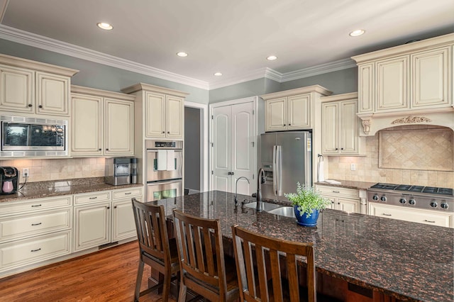 kitchen featuring cream cabinets, stainless steel appliances, a kitchen breakfast bar, and dark stone countertops