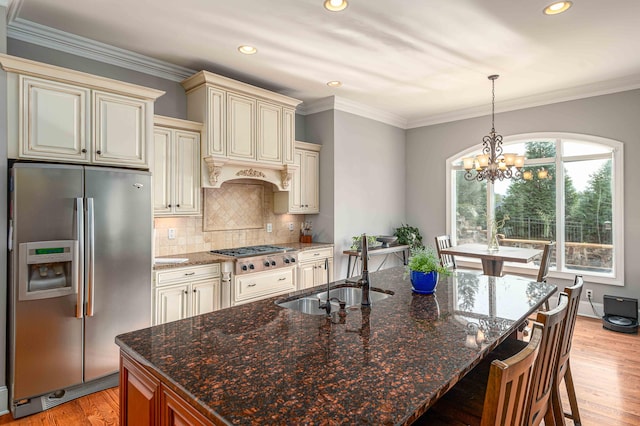 kitchen featuring decorative backsplash, appliances with stainless steel finishes, an inviting chandelier, dark stone countertops, and cream cabinetry