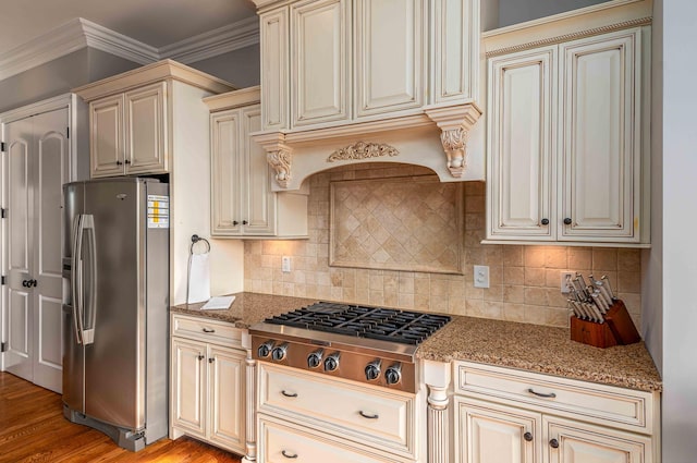 kitchen with appliances with stainless steel finishes, backsplash, cream cabinets, stone countertops, and light hardwood / wood-style floors