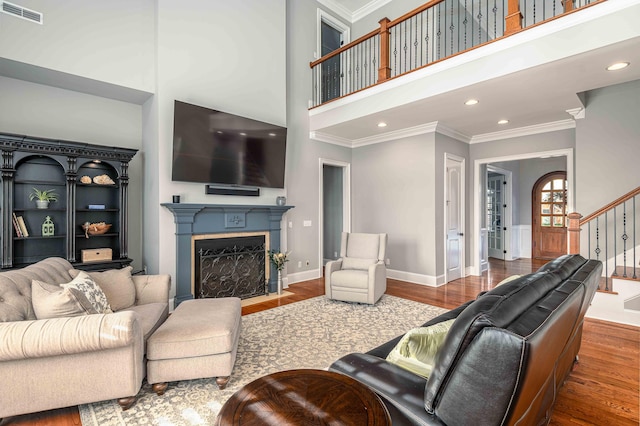 living room featuring wood-type flooring, crown molding, and a high ceiling