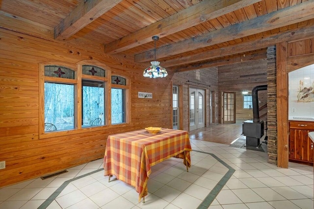 tiled dining space featuring beam ceiling, a wood stove, wooden walls, and wood ceiling