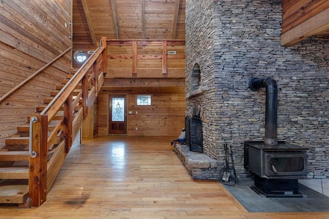 unfurnished living room with wooden ceiling, a high ceiling, wooden walls, beamed ceiling, and light hardwood / wood-style floors