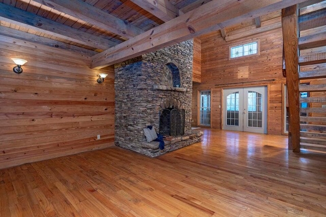 unfurnished living room featuring french doors, light wood-type flooring, beamed ceiling, plenty of natural light, and wood ceiling