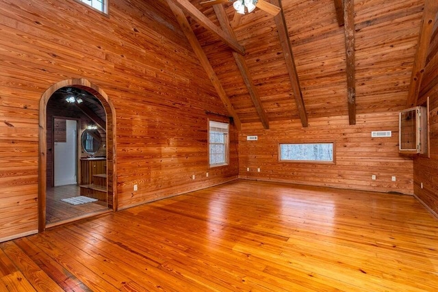 unfurnished living room featuring light wood-type flooring, wood ceiling, ceiling fan, wooden walls, and vaulted ceiling with beams