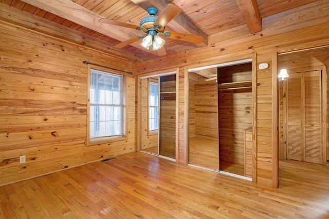 unfurnished bedroom with wooden walls, light wood-type flooring, beam ceiling, wood ceiling, and multiple closets